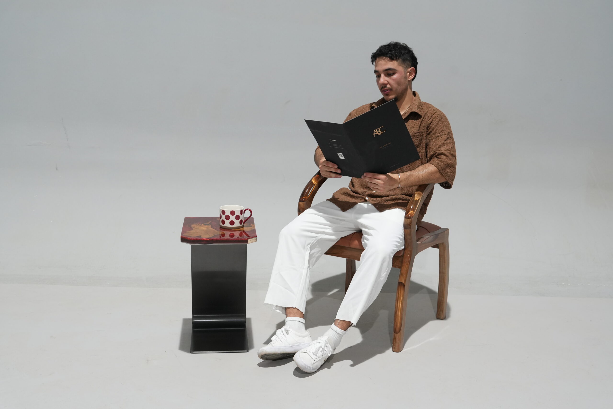 A man sitting on a chair reading with the Crimson Olive Root Side Table beside him, displaying its use in a living space.