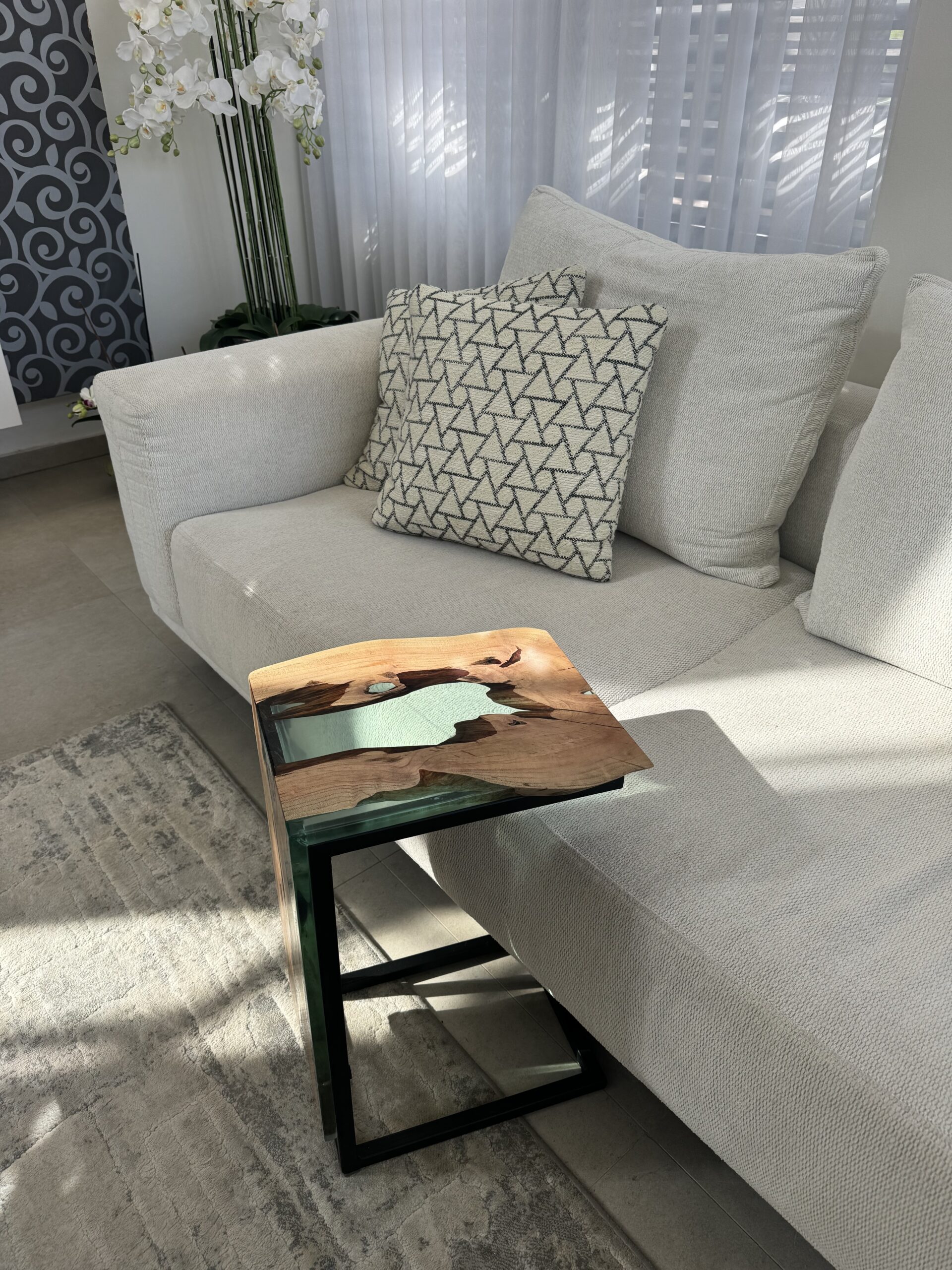 Carob wood side table positioned beside a light grey sofa, with decorative pillows.