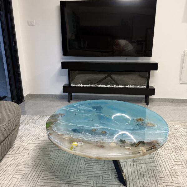 A coffee table featuring a serene coastal design in epoxy resin, showing shells and a miniature beach within a clear surface.